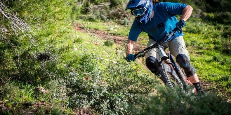 Mountain biker wearing helmet and goggles rides down a rough forest trail during daytime