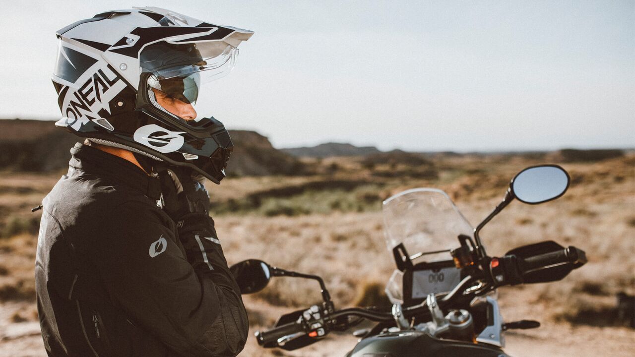 Man on motorbike straps up O'Neal Sierra RV.22 off-road helmet with desert backdrop