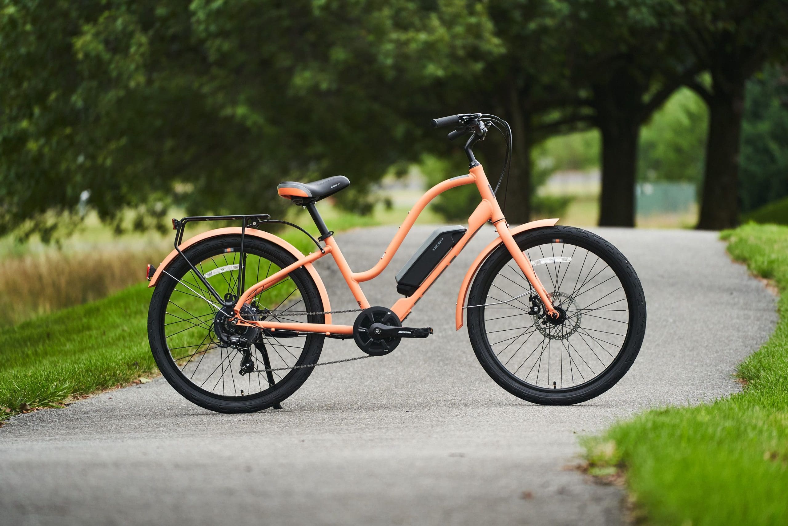 Peach coloured SIMI STEP THRU electric cruiser bike rests on kickstand on forest trail