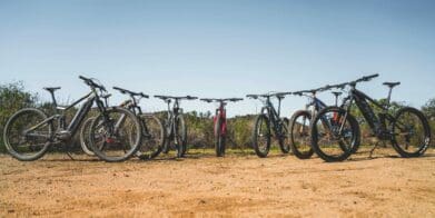 Collection of multiple electric mountain bike models lined up outside on rough terrain