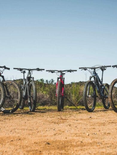 Collection of multiple electric mountain bike models lined up outside on rough terrain