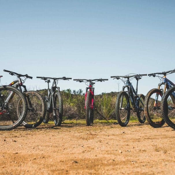 Collection of multiple electric mountain bike models lined up outside on rough terrain