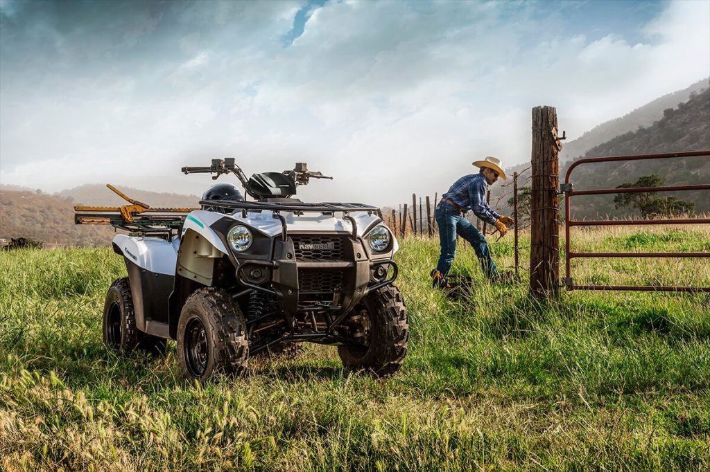An image of a man fixing a fence with his Kawasaki Brute Force 300 in the foreground