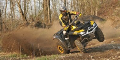 Rider in gear on yellow ATV tilting sideways in forest