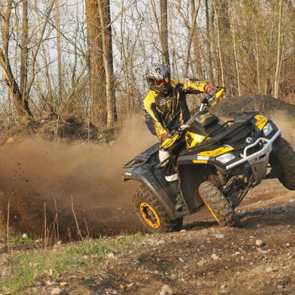 Rider in gear on yellow ATV tilting sideways in forest