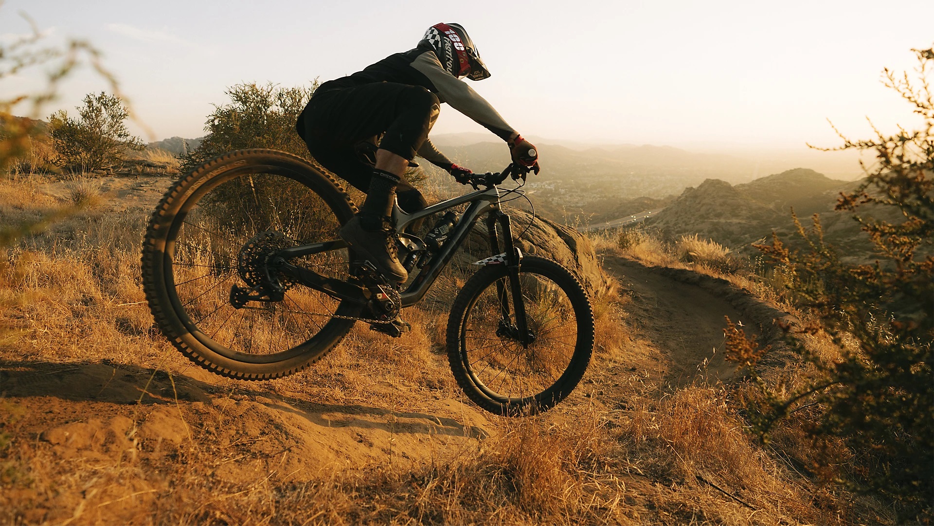 Electric mountain biker rides downhill dirt trail in dry mountainous environment