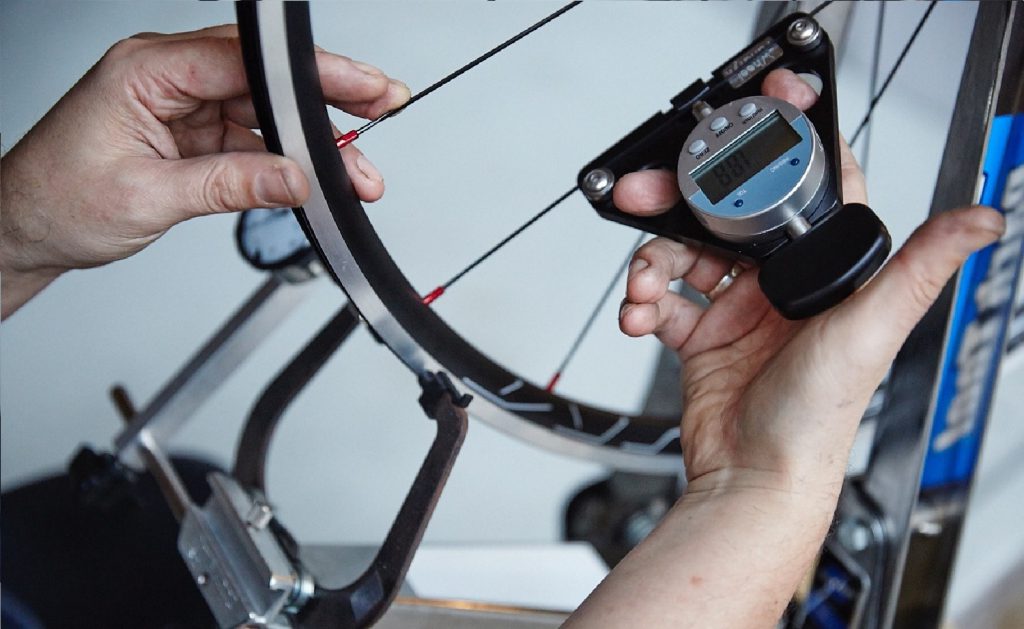 Man adjusts the spokes of a bicycle wheel with a spoke key