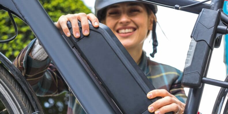 Smiling woman fits removable lithium-ion battery pack to her electric bike