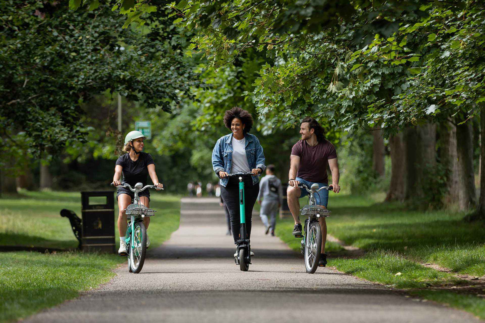 Woman rides her electric scooter through park with two friends on bicycles