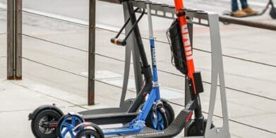 Three electric scooters locked onto a stand within inner-city