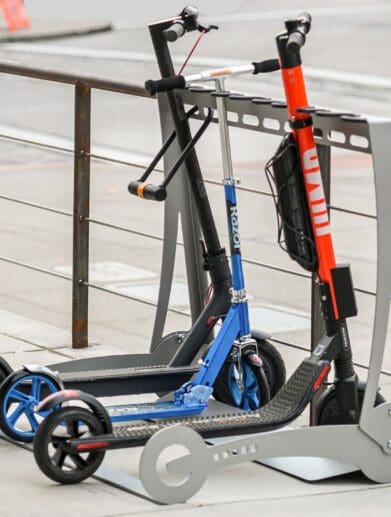Three electric scooters locked onto a stand within inner-city