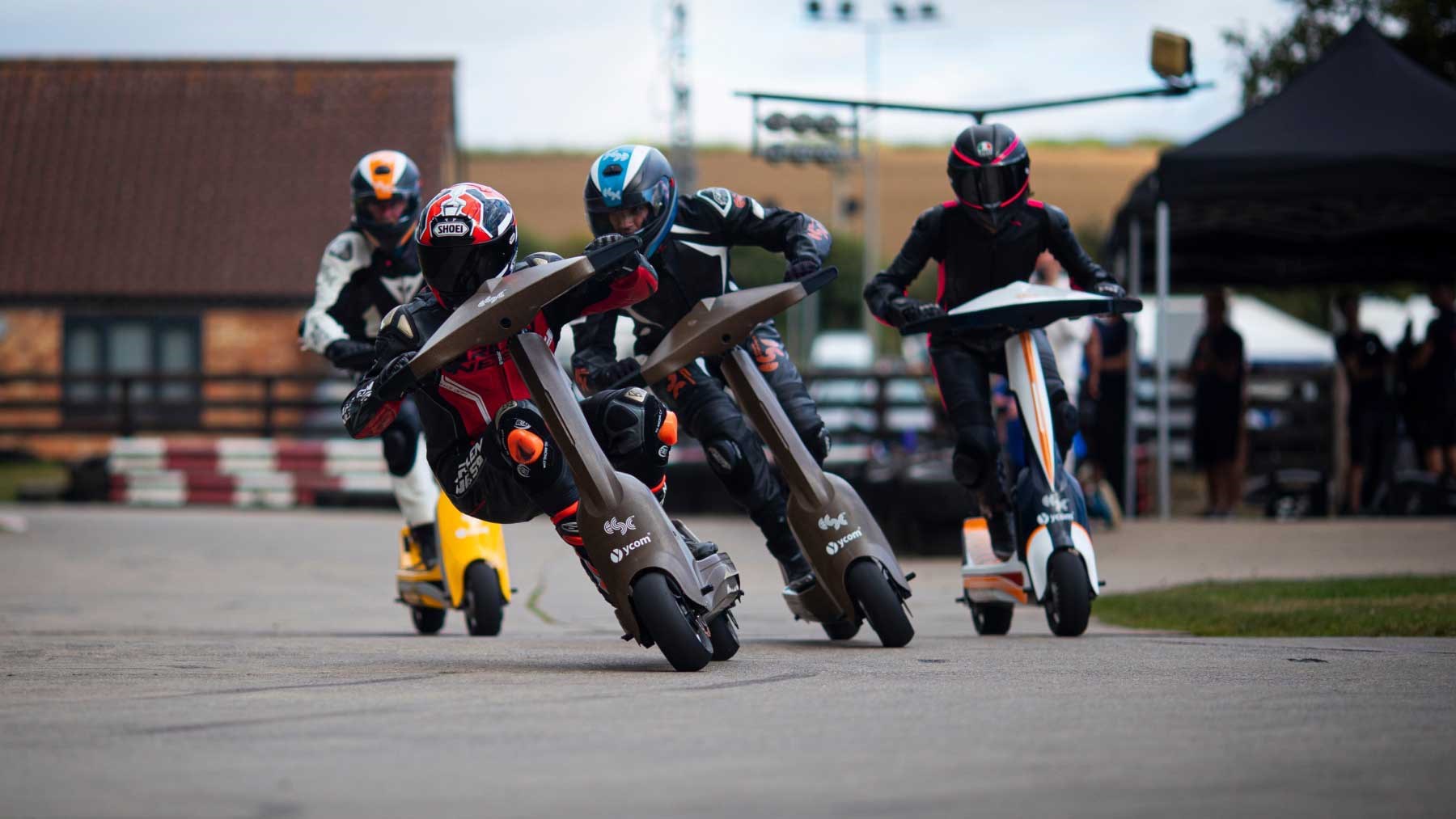 Group of competitive electric scooter racers wearing body armour turning corner at speed during race