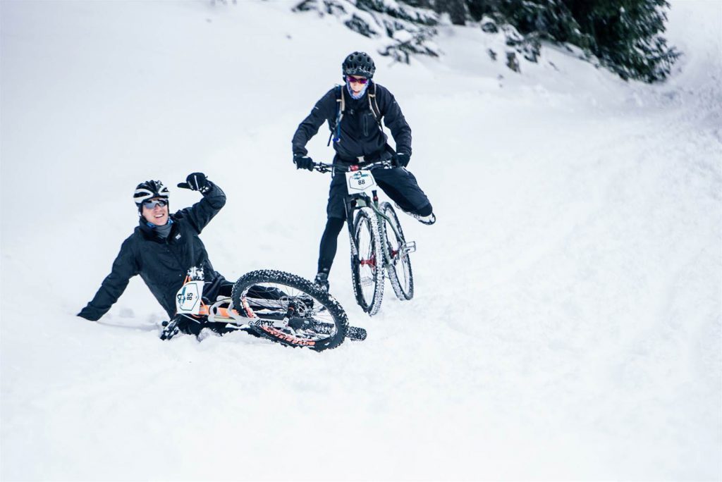 Female cyclist stops near a fallen cyclist in heavy snow