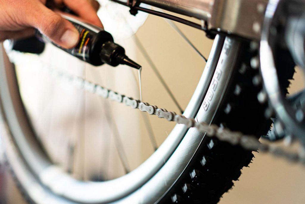 Close-up of a man applying wet lubricant to a bicycle chain