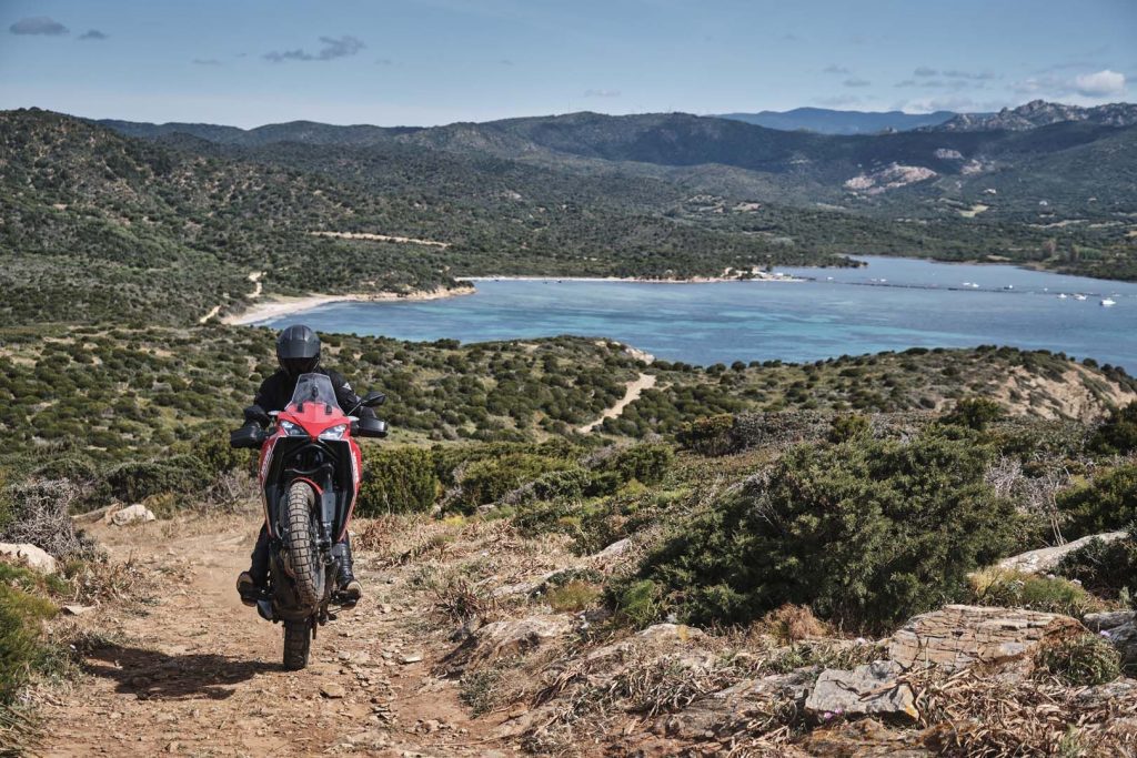 A view of a rider trying out the all-new Moto Morini X-Cape adventure motorbike on rugged terrain, with a gorgeous tropical view.