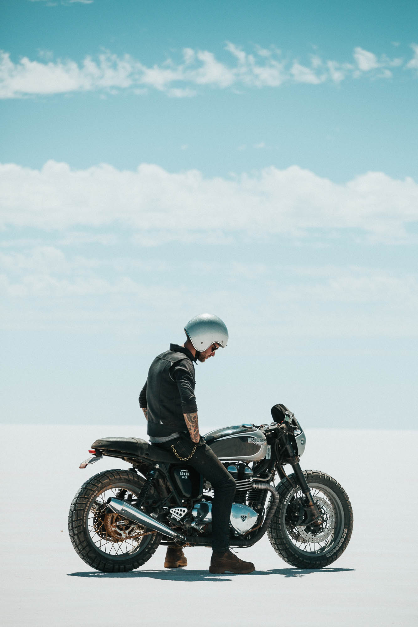 A man sits on a custom Triumph Motorcycle on a salt flat in Australia