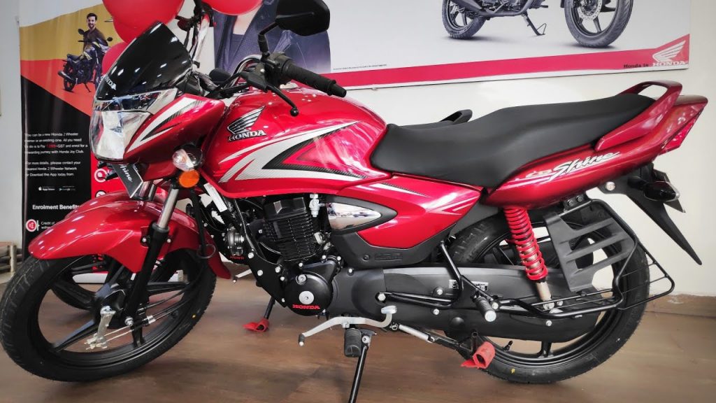 The Honda Shine, in red, rolled out on a wooden floor in front of a Honda poster.