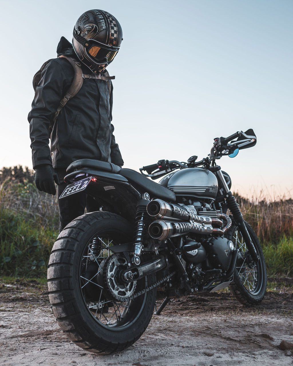 Motorcycle rider stand next to their Triumph Scrambler at dusk