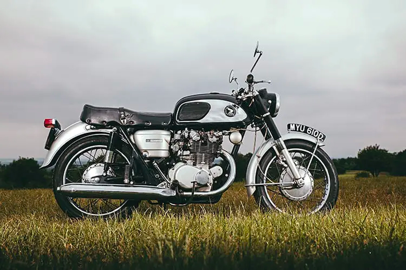 A classic Honda CB450 Black Bomber motorcycle is parked on grass at dusk on a cloudy day