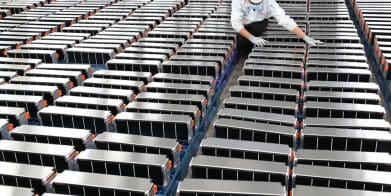 A view of a worker aligning a series of EV batteries. Media sourced from Energy Monitor.