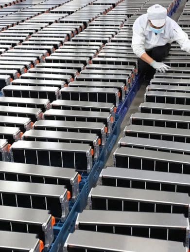 A view of a worker aligning a series of EV batteries. Media sourced from Energy Monitor.