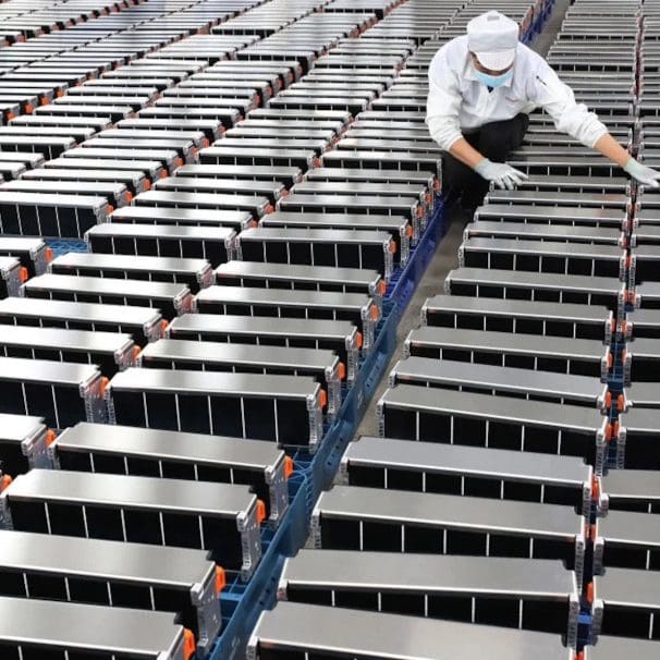 A view of a worker aligning a series of EV batteries. Media sourced from Energy Monitor.