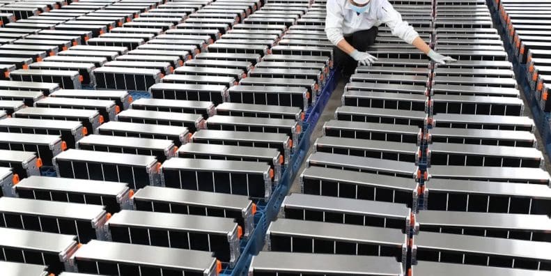 A view of a worker aligning a series of EV batteries. Media sourced from Energy Monitor.