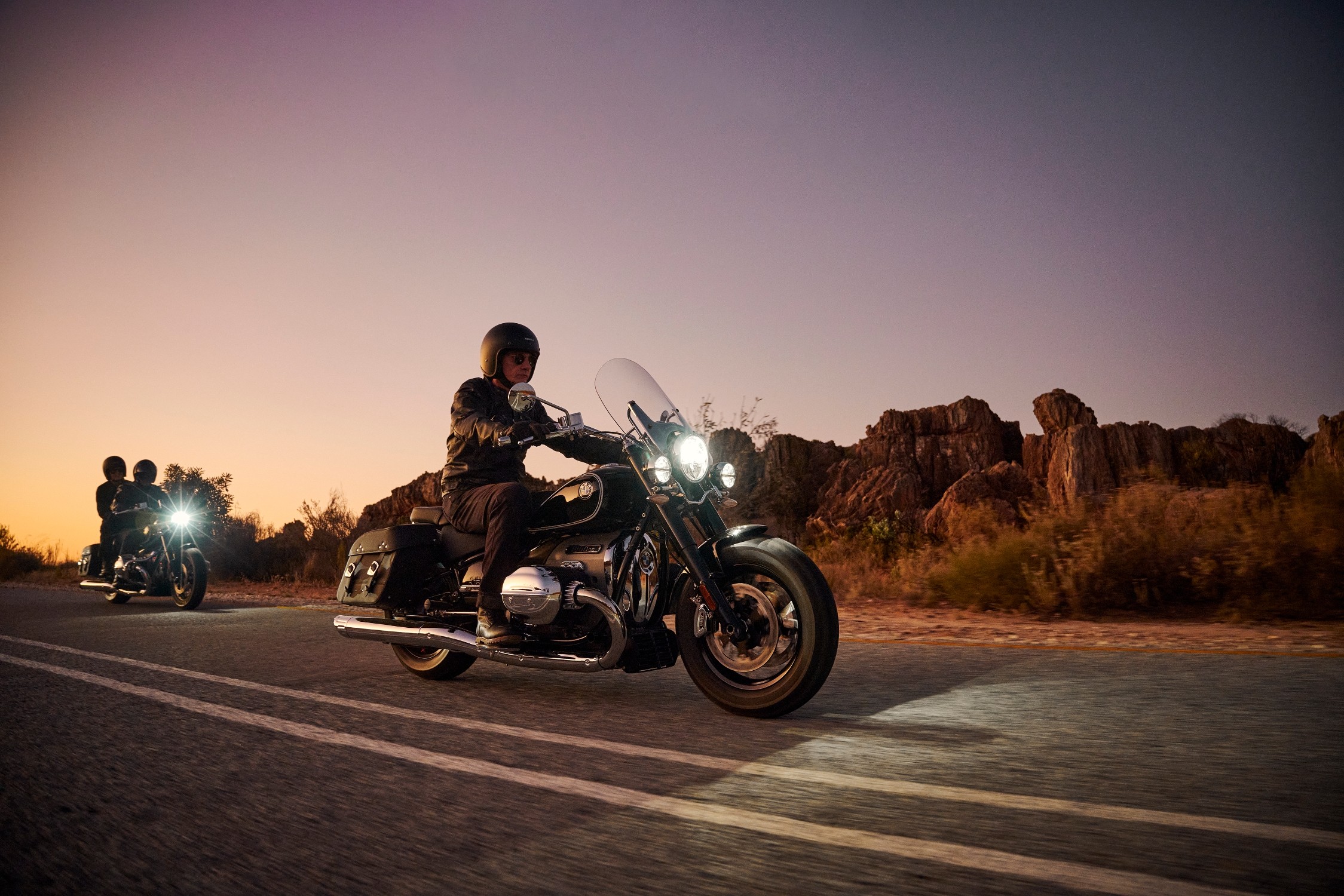 A man rides an R 18 motorcycle at dusk in the desert