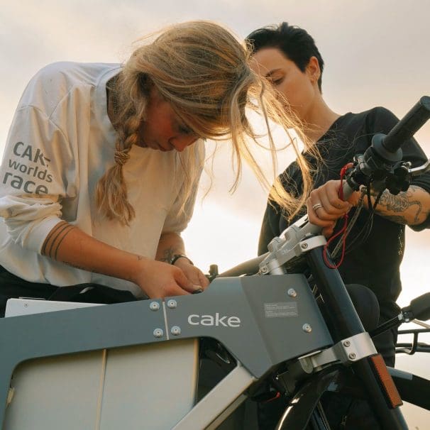 Two girls bending over an electric motorcycle.