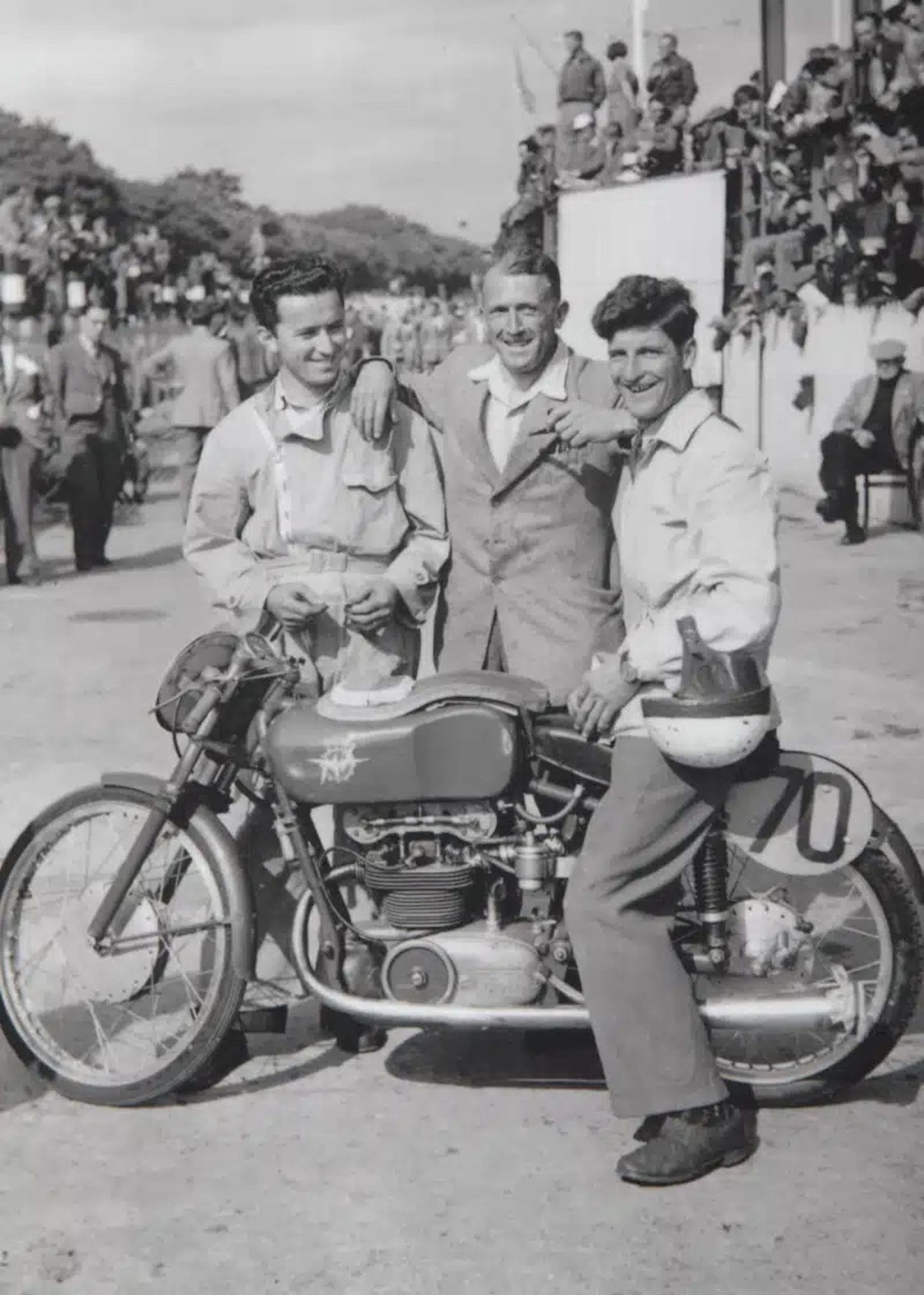 A vintage photograph showing three men around a winning motorcycle.