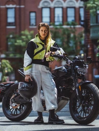 A woman standing in front of an electric motorcycle.