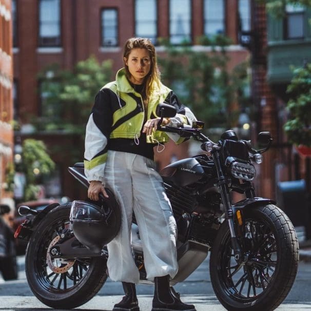 A woman standing in front of an electric motorcycle.