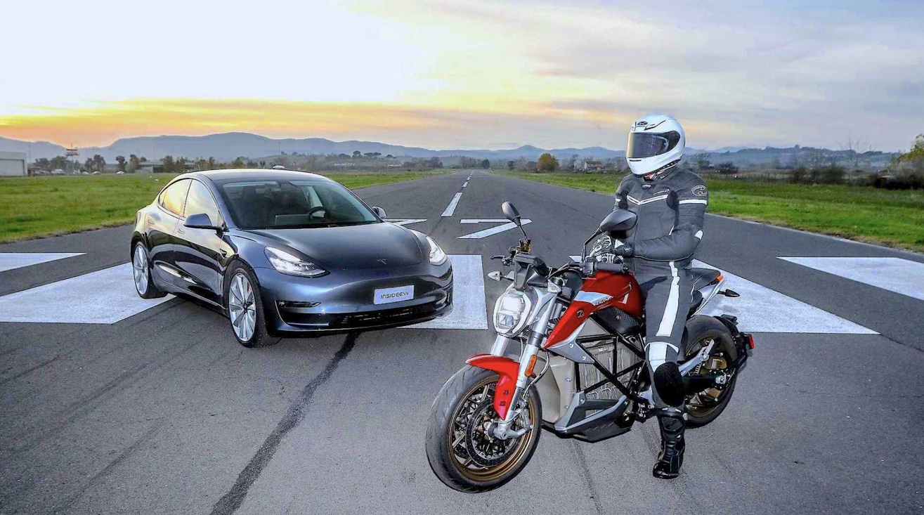 A Tesla car behind a naked electric motorcycle with a rider.