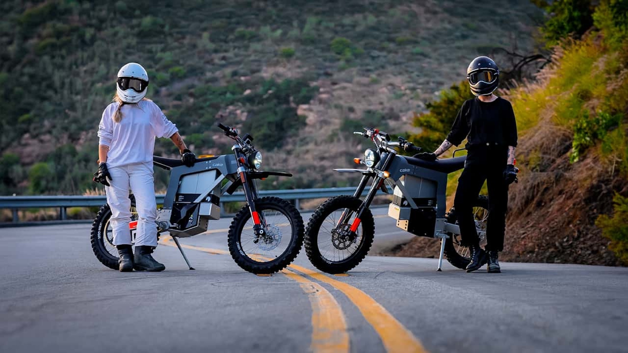 two girls in helmets next to electric motorcycles.