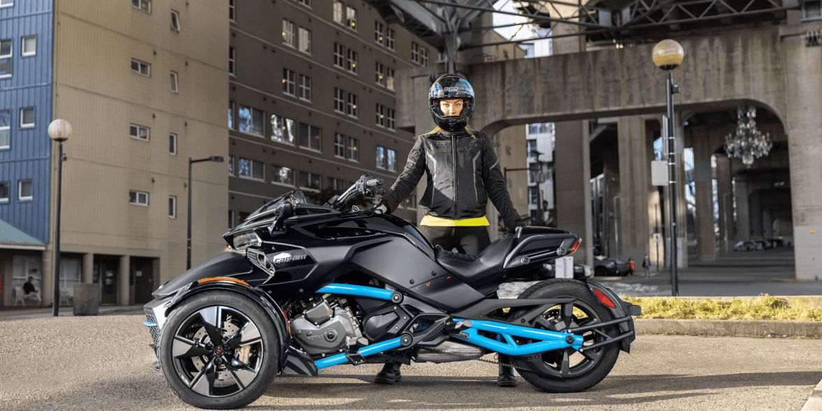 A woman in motorcycle gear standing behind a motorcycle.