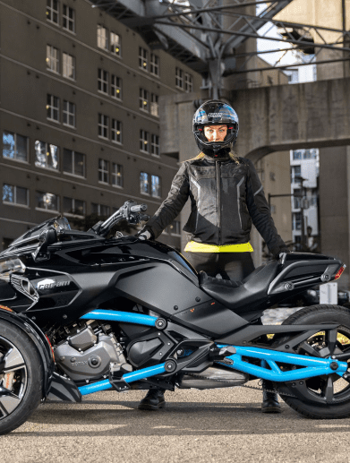 A woman in motorcycle gear standing behind a motorcycle.