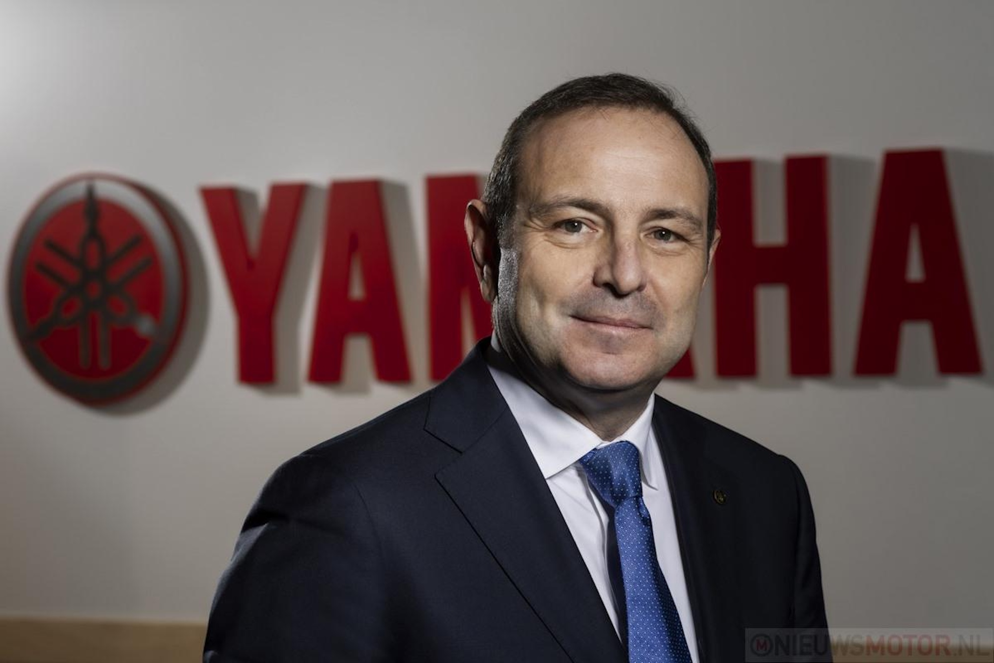 A man in a suit in front of a logo.