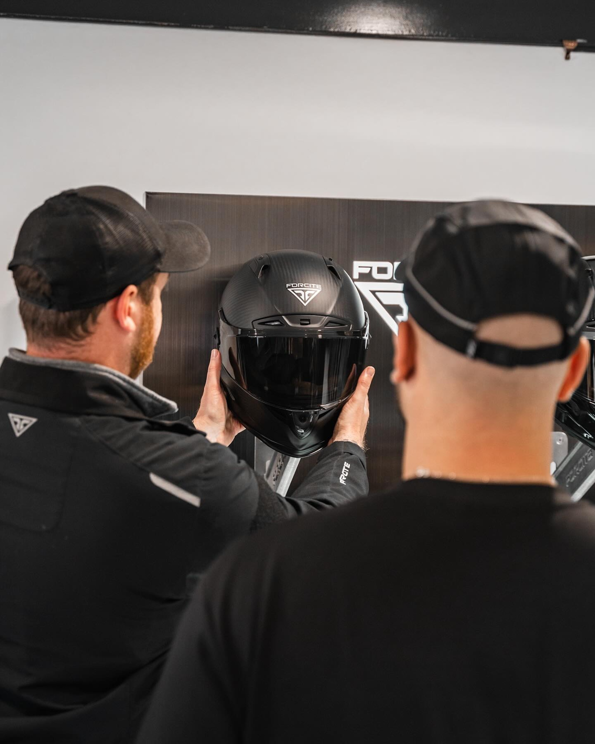 Two men picking up a motorcycle helmet.