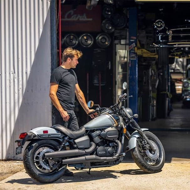 A guy standing behind a cuiser bike.