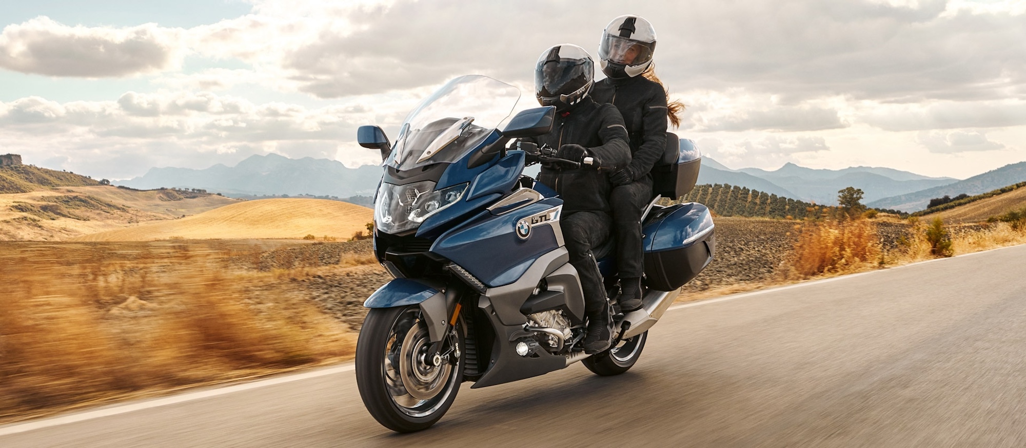 Two motorcyclists riding on a cloudy day.