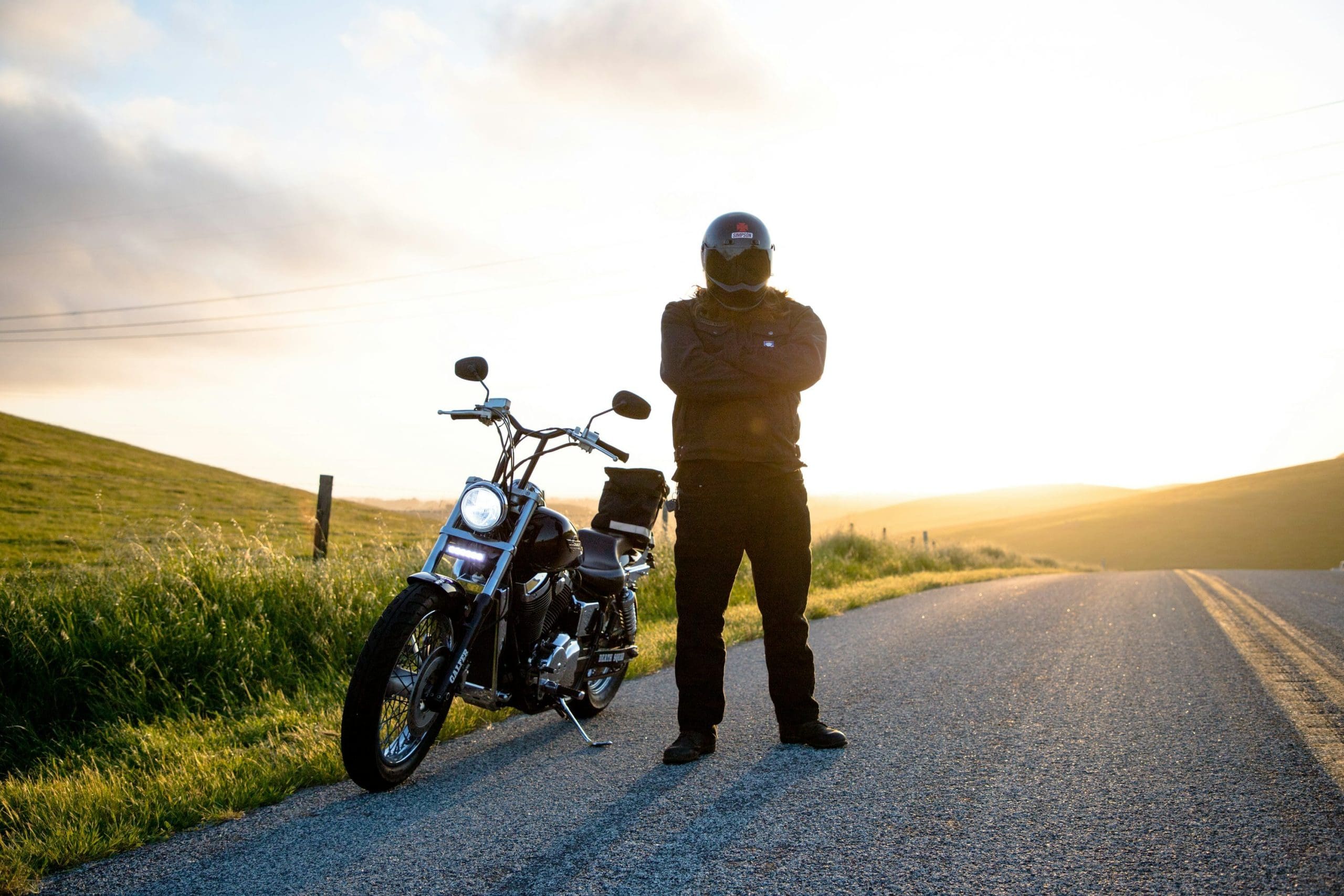 A man with a helmet standing beside a motorcycle on the side of a road