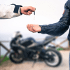 A person handing over the keys of a motorcycle with a black bike in the background
