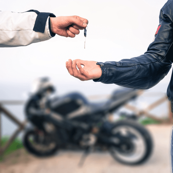 A person handing over the keys of a motorcycle with a black bike in the background