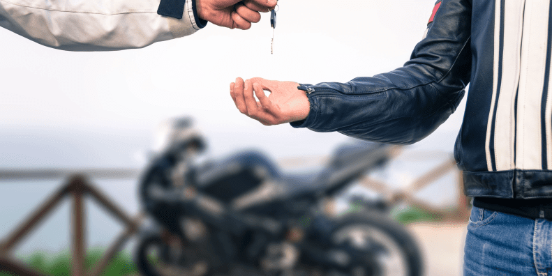 A person handing over the keys of a motorcycle with a black bike in the background
